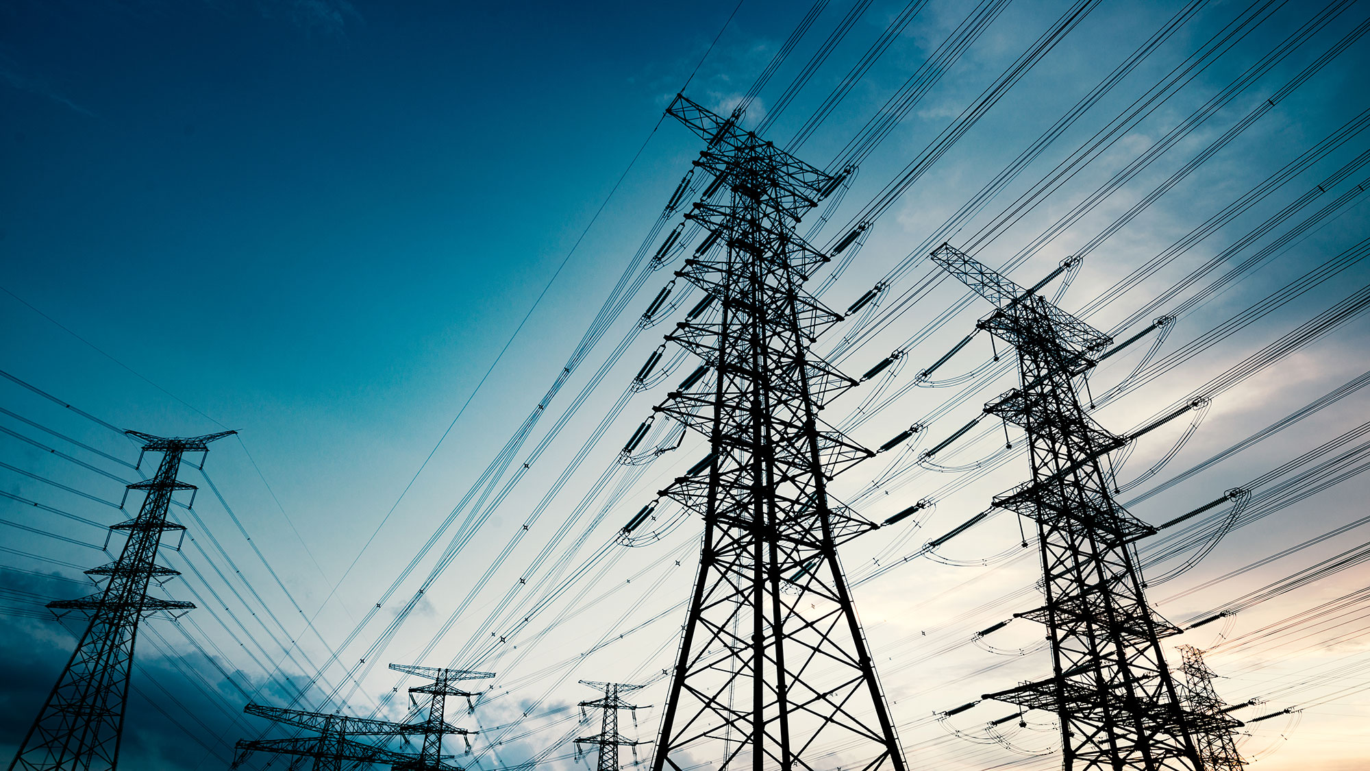 Electricity transmission towers silhouetted against a colourful sky