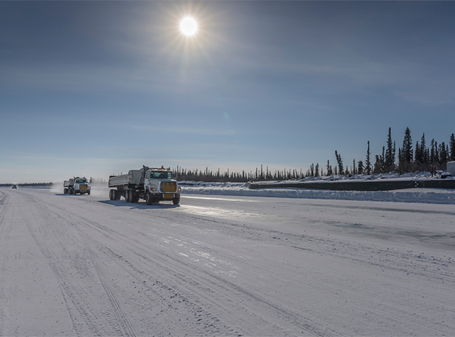 Construction trucks driving on a road in northern Canada